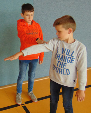 Zwei Jungen führen ein Hebel-Experiment durch, einer drückt den Arm des anderen nach unten.